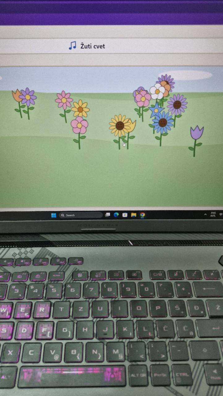 Ekran laptopa prikazuje zelenu površinu sa raznobojnim stilizovanim cvetovima. Iznad scene stoje simbol note i tekst „Žuti cvet“; fotografija ne prenosi zvuk ili tok interakcije.