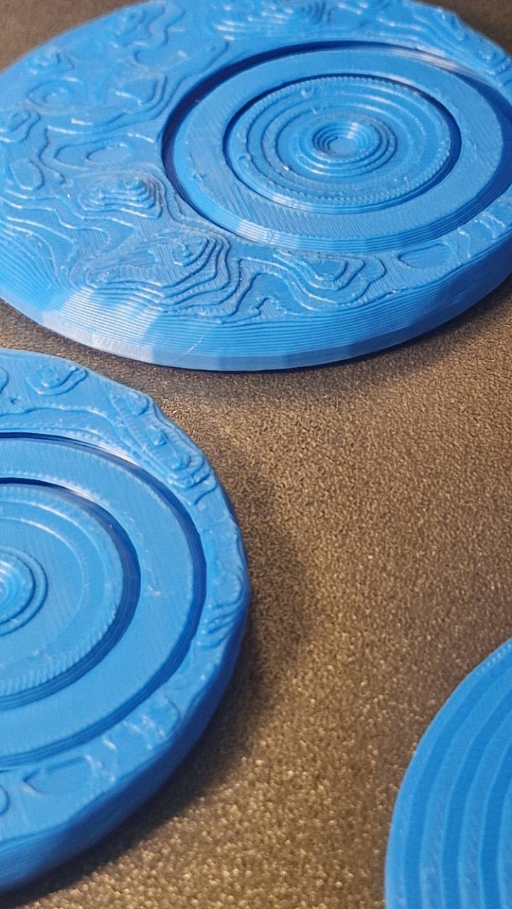 Plavi kružni 3D štampani elementi sa koncentričnim prstenovima i reljefnim detaljima na podlozi štampača.